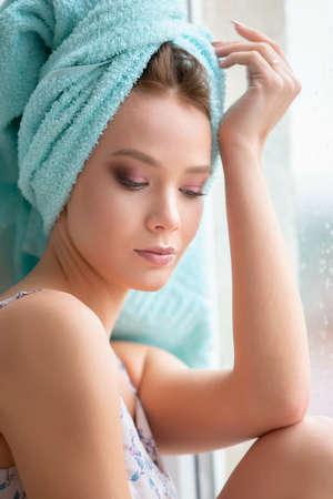 Beautiful girl after a shower in a towel sits at the window.の写真素材