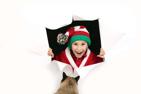 Child Santa Claus from a hole in paper rejoices to a cat