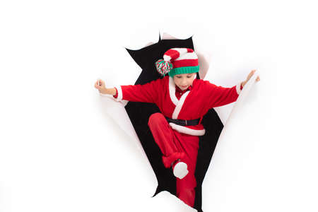 Child Santa Claus comes out of a hole in paper. A boy in a New Years costume is smiling. Holiday...