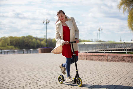 An adult woman is riding a scooter on the street. Active middle-aged woman on a walk.の写真素材