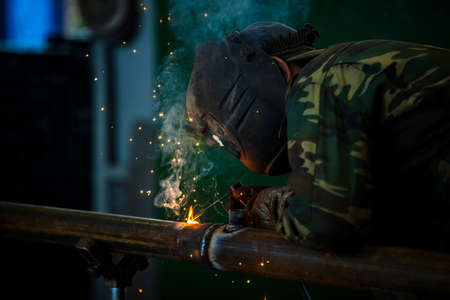 Welder at work. Man in a protective mask. The welder makes seams on the metal. Sparks and smoke when...
