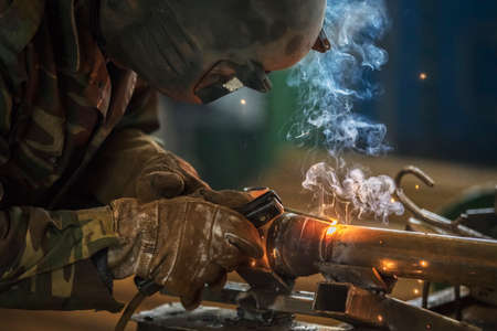 Welder at work. Man in a protective mask. The welder makes seams on the metal. Sparks and smoke when...
