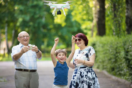 Happy elderly couple with a grandson on a walk. An elderly husband and wife and child launch a drone.の写真素材