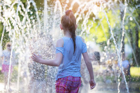 Wet girl looks at the fountain. Child on a hot day at the city fountain.の写真素材