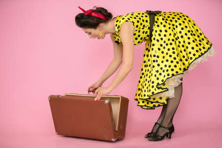 Retro girl opens an old suitcase on a pink background.