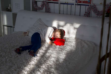 The boy is lying on a white bed. Preschooler tiredの写真素材