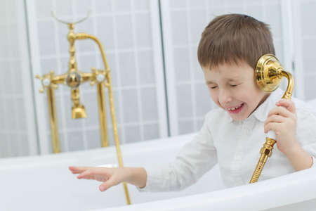 Baby in the bathroom in clothes.The boy sits in the bath and plays the phone.Talking on the phone