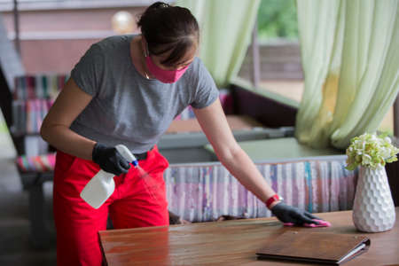 Waiter wearing protective face mask while disinfecting tables at outdoor cafe