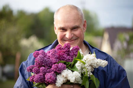 Elderly man with a bouquet of flowers. Brutal gray-haired man with a beautiful lilac.