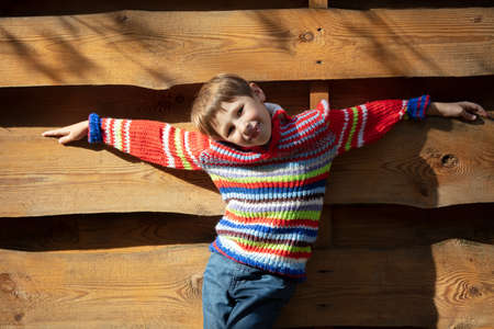 Beautiful baby in nature. Elementary age boy on the background of a wooden fence. Autumn walk of the child.の写真素材