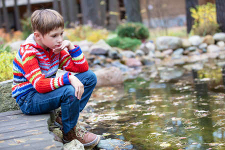 Child on an autumn walk. Sad boy by the lake.の写真素材