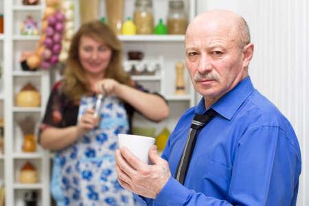Elderly man with a cup on the background of his wifeの写真素材