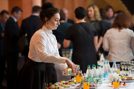 Belarus, Vitebsk, February 27, 2019. City restaurant. Food festival Waiter with a tray.A woman bartender is laid on the table. The waitress is working.のeditorial素材