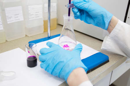 The hands of a technician in blue rubber gloves are holding a flask. Pharmaceutical industry....