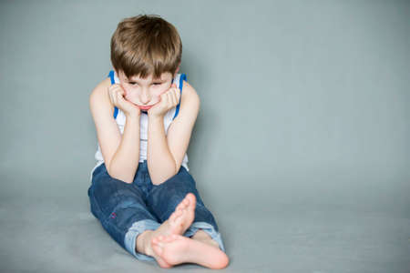 Sad preschooler sitting on the floor. A bored child. Upset little boy.の写真素材