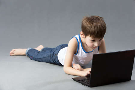 Child with a computer. The boy is lying on the floor with a laptop