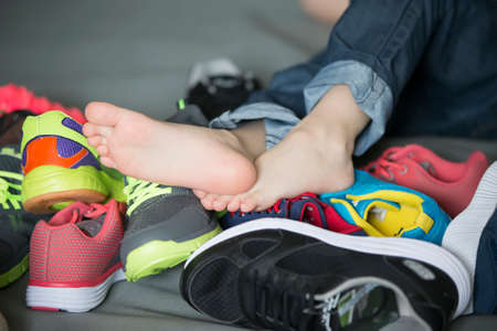 Bare feet in a pile of shoes. Childrens foot on the background of sneakers. Foot and shoesの写真素材