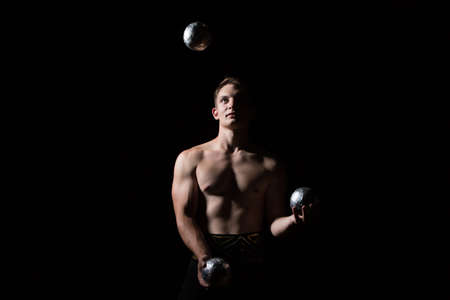 Handsome guy with a muscular body juggles with heavy balls on a black background.Power jugglerの写真素材