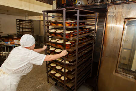 Belarus, the city of Gomil, April 25, 2019. Bakery.A bakery worker places trays with raw bread in the oven. Industrial production of bakery products.のeditorial素材