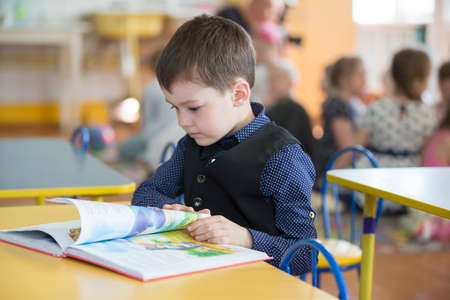 Belarus, the city of Gomel, April 26, 2019. Open day in kindergarten. The boy is a preschooler. Portrait of a six year old child with a book. Junior student at a desk.のeditorial素材