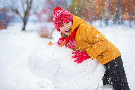 Child in winter. A happy boy in bright clothes plays in the snow.