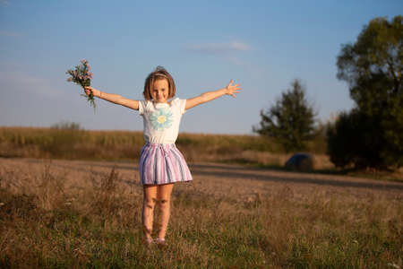 Beautiful little girl in the meadow with a bouquet of flowers. A child in a beautiful summer field.の写真素材