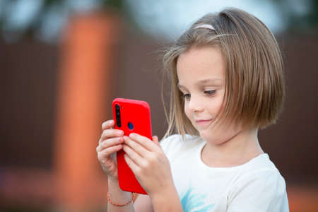 Child with a smartphone. The little girl is talking with a red phone.の写真素材