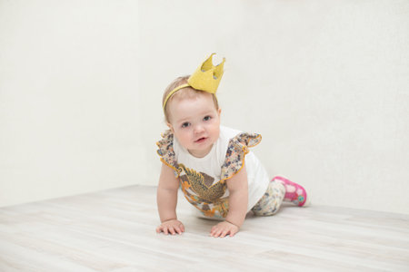 A one-year-old girl with a crown. The little princess crawls on the floorの写真素材