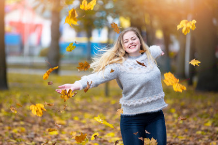 Beautiful girl in the autumn park scatters yellow leaves.の写真素材