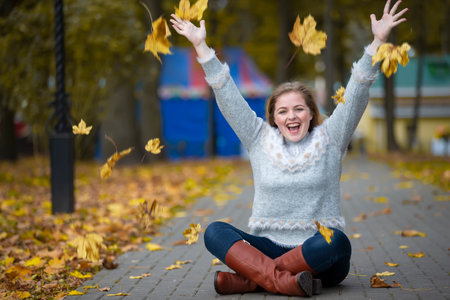 Beautiful girl in the autumn park scatters yellow leaves.の写真素材