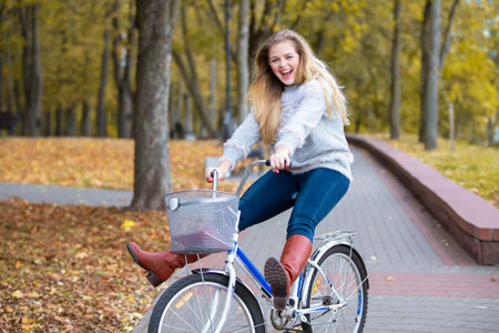 Young beautiful woman rides a bicycle in the autumn park.の写真素材