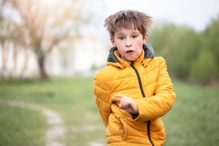 A child in a yellow jacket runs against the backdrop of greenery.の写真素材