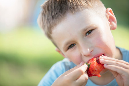 The child eats berries. The face of a boy eating sweet strawberries.の写真素材
