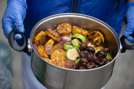 The chef's hands are holding a saucepan with grilled vegetables and mushrooms.の写真素材