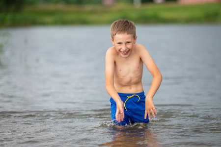 A little boy runs into a cold river. The child swims in the lake in summer.の写真素材