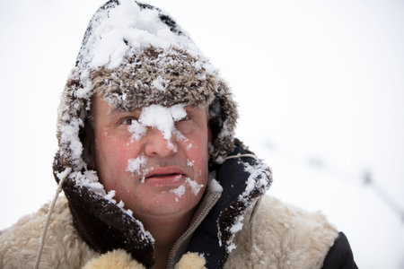 The frozen man in winter snow fell on his face. The first snow fell. A man in a fur hat in cold weather.の写真素材