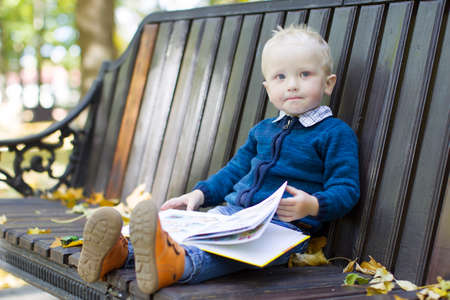 Toddler in the park on a bench with a book. Two-year-old child turns the pagesの写真素材