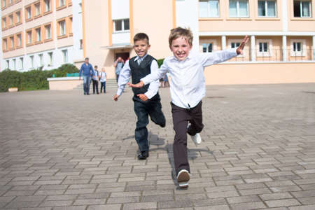 Boys schoolchildren are running along the road. Joyful children in the background of the school.The boy is running.End of the school year. Beginning of summer holidays at schoolの写真素材