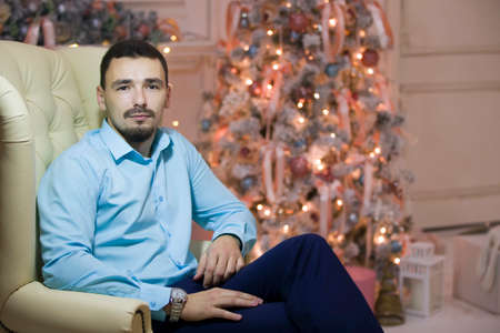 A man in a leather chair on the background of the Christmas tree