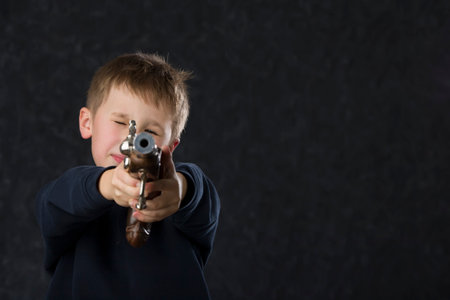 Boy with a gun. The child plays with the weapon. Six seven year old kid aiming a gun