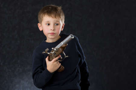 Boy with a gun. The child plays with the weapon. Six seven year old toddler with retro boob