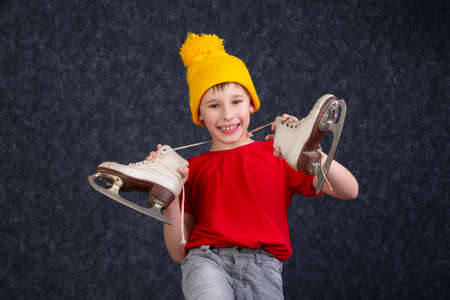 Handsome little boy in a knitted yellow hat with vintage skates on a gray background.の写真素材