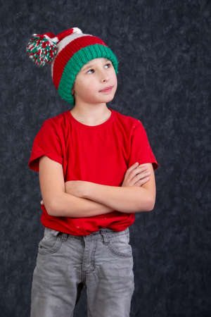 Funny little boy in a knitted Christmas hat on a gray background.の写真素材
