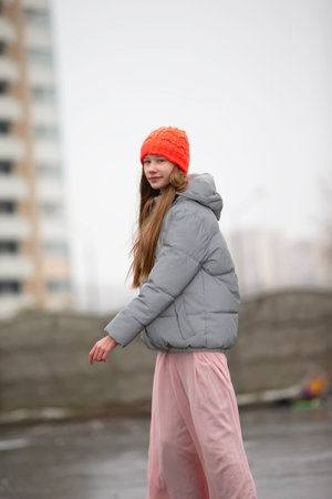 Teenage girl in a knitted hat and warm jacket against the backdrop of the city.の写真素材