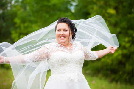 Portrait of a plump bride with a waving veil against a background of summer greenery.の写真素材