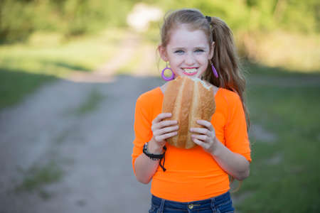 Happy little girl on the street eating a bun.の写真素材