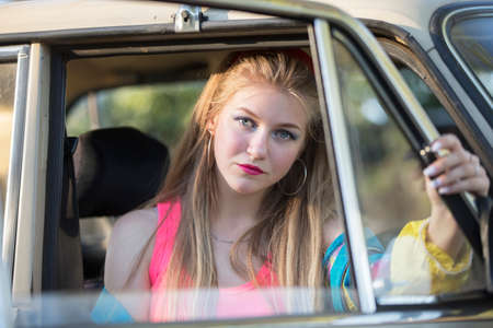 A beautiful blonde girl with long hair looks out of the car window.