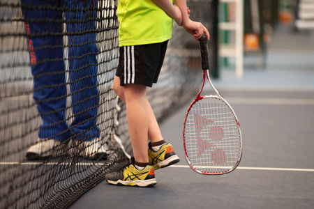 April 01, 2021. Belarus, the city of Gomil. Children's competitions in big tennis. Children's feet in sneakers with a big tennis racket.のeditorial素材