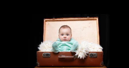 A little kid sits in a retro suitcase and looks at the camera. Funny baby. The boy is four months old.の写真素材