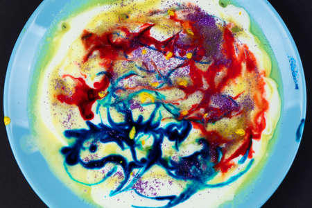 On a white plate, smeared ink multicolored paints on a black background. An abstract work of art....